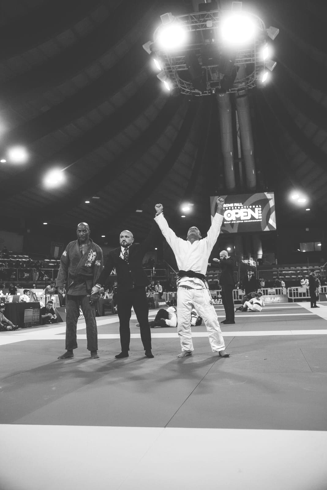 Il maestro con le braccia alzate al centro del tatami, sotto le luci della gara